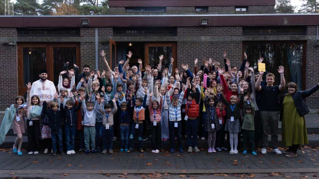 Grup mare de copii și adolescenți pozând cu mâinile ridicate în fața unei clădiri